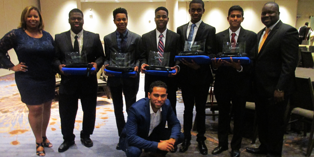 Group photo of seven individuals, including five young men in formal attire holding awards, one woman and one man standing beside them, taken at a celebratory event.